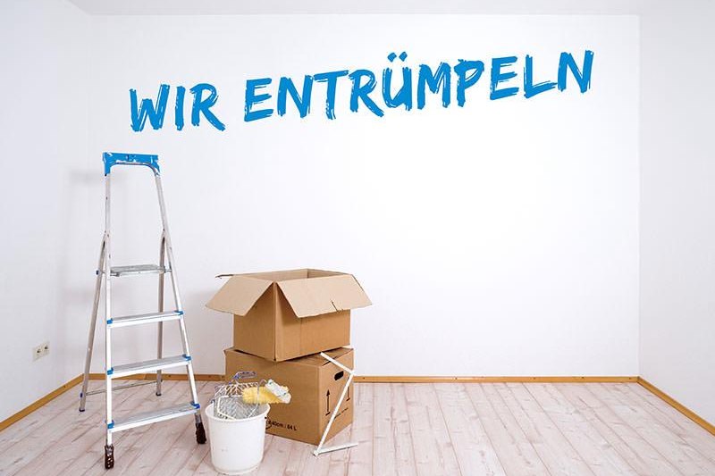 Leergeräumter Raum mit Leiter und Umzugskartons und dem Schriftzug „Wir entrümpeln" an der Wand
